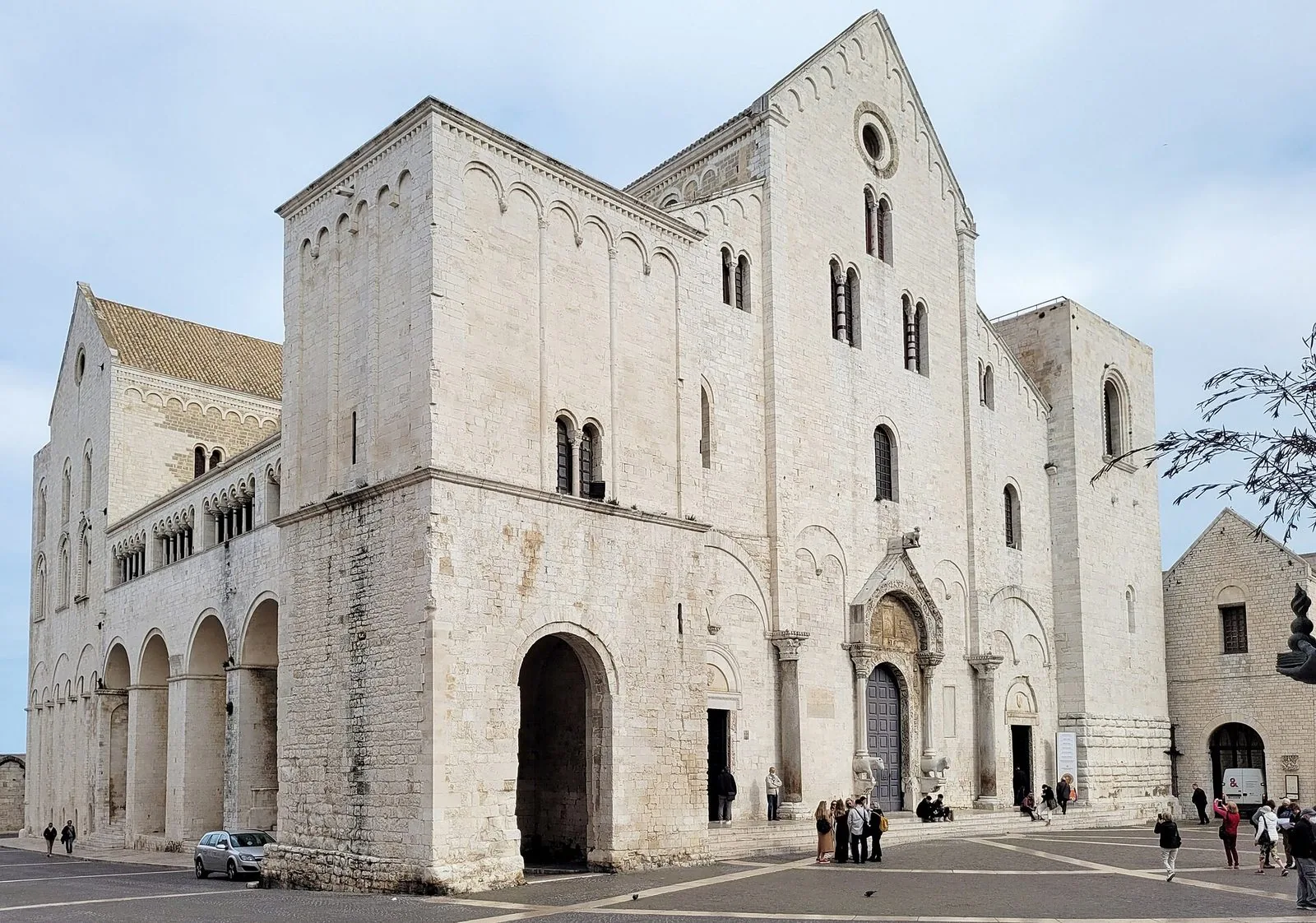 La facciata in pietra chiara della Basilica di San Nicola a Bari, vista di scorcio dalla piazza sotto un cielo nuvoloso