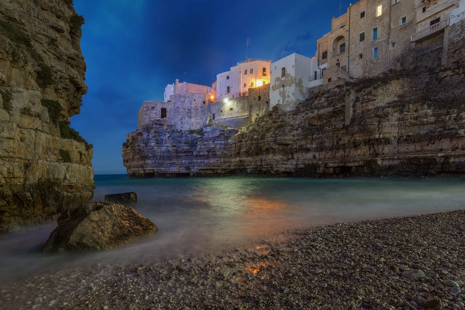 La spiaggia di ciottoli di Lama Monachile a Polignano a Mare all’imbrunire, con le case illuminate sopra la scogliera