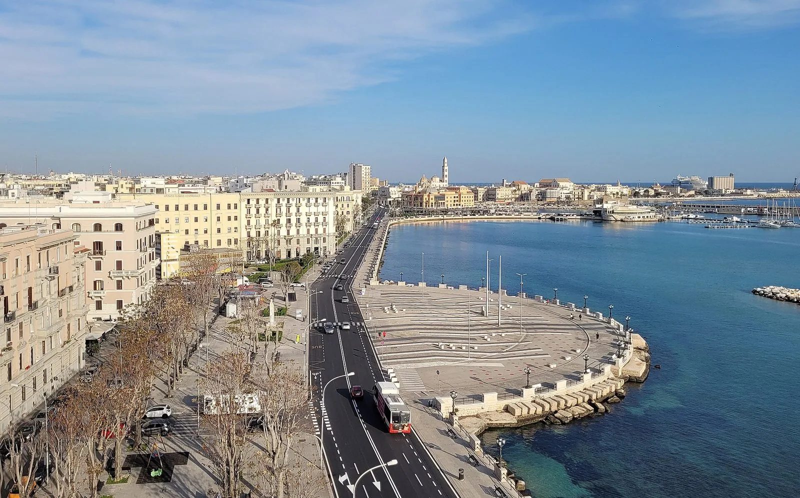 Il lungomare di Bari visto dall'alto, con la passeggiata sul mare, la piazza affacciata sull'acqua e sullo sfondo il porto e il profilo di Bari Vecchia con il campanile