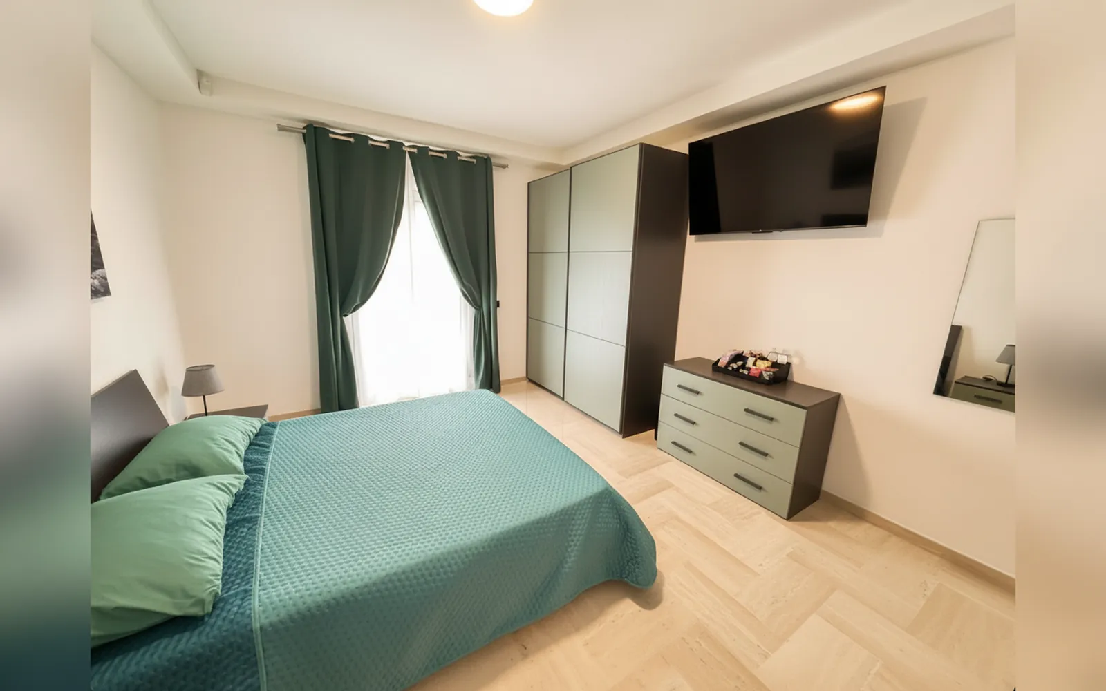 Il letto matrimoniale con il copriletto verde acqua e l’armadio grigio